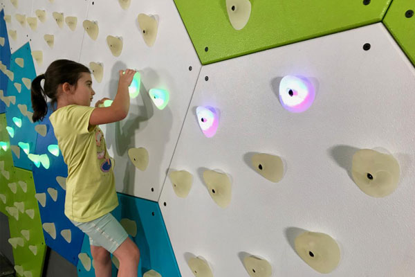 Young girl climbing GlowHolds wall with safety matting